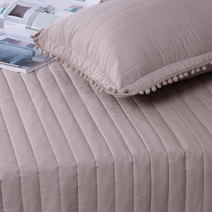 Quilted bedspread with a pillow on a bed, featuring a soft texture and neutral color.