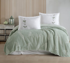 Green textured comforter and pillows on a bed in a bedroom setting.